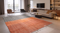 Ouarzazate Terracotta two-tone handwoven kilim rug in a modern living room, rust orange and grey fields with fringed edges.