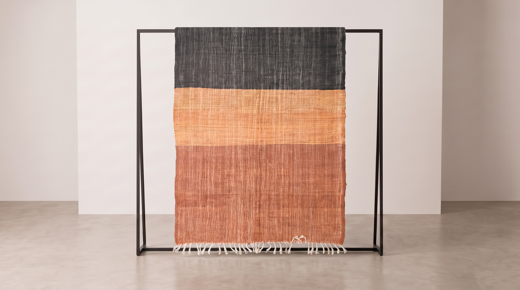 Ouarzazate Terracotta kilim rug detail, two-tone charcoal and terracotta orange handwoven wool with fringed edge, displayed on a stand in a studio.