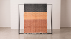 Ouarzazate Terracotta kilim rug detail, two-tone charcoal and terracotta orange handwoven wool with fringed edge, displayed on a stand in a studio.