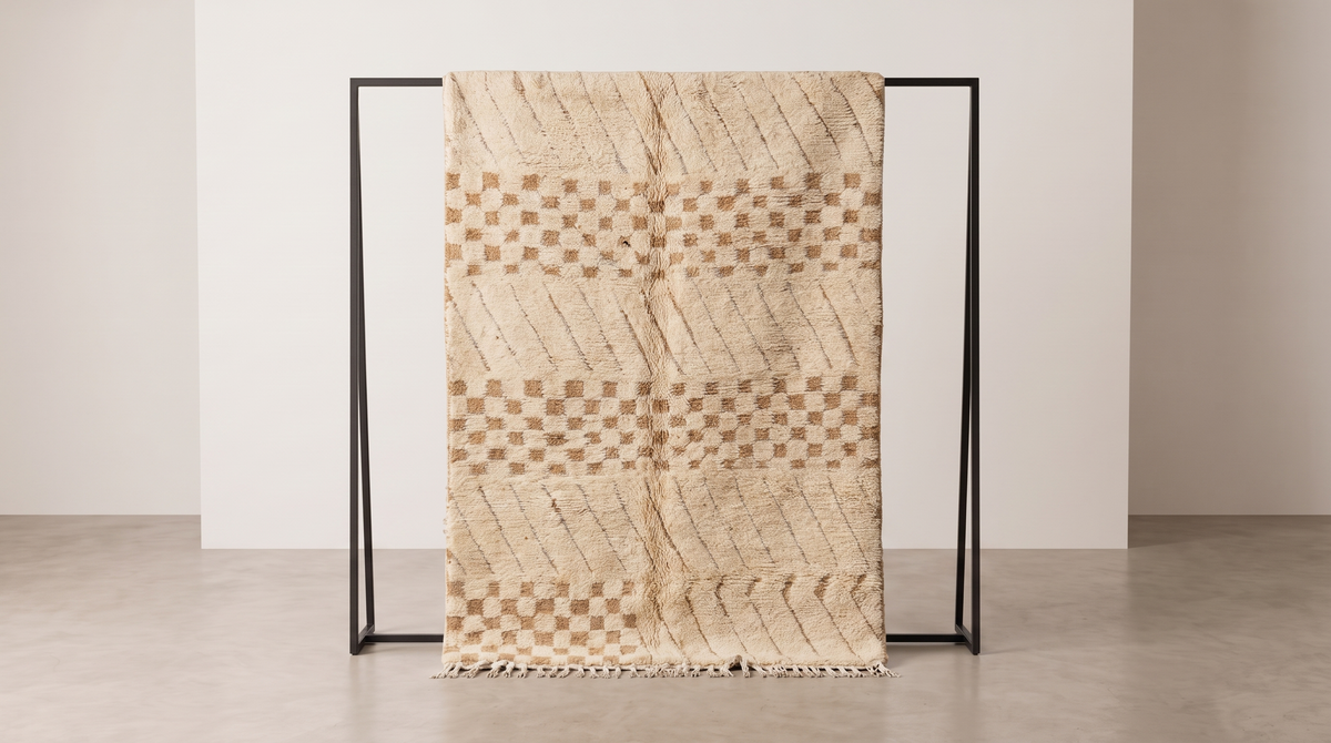A woven throw blanket with a beige and brown geometric pattern is draped over a minimalist black metal stand in a clean, modern room setting.